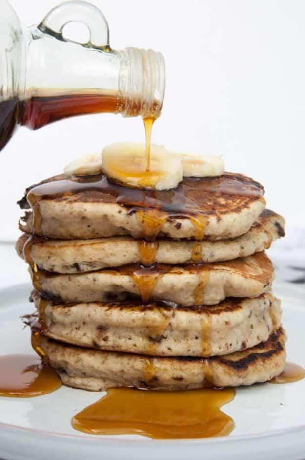Vegan banana bread pancakes stacked with banana slices on top and maple syrup poured over the whole stack