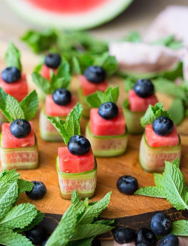 Watermelon canapes made of cubed watermelon wrapped in cucumber ribbons with mint and a blueberry on top