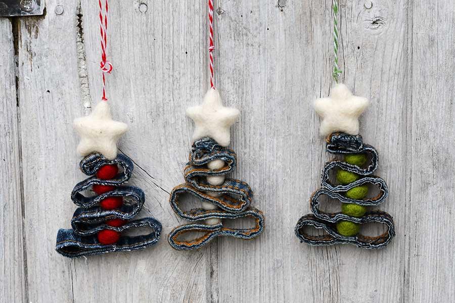 Three Christmas tree ornaments made from zigzagged denim seams with colorful felt balls and white felt stars on white wood