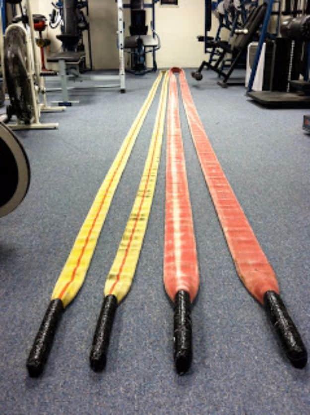 Four lengths of yellow and red decommissioned fire hose laid flat on a gym floor with black taped handles