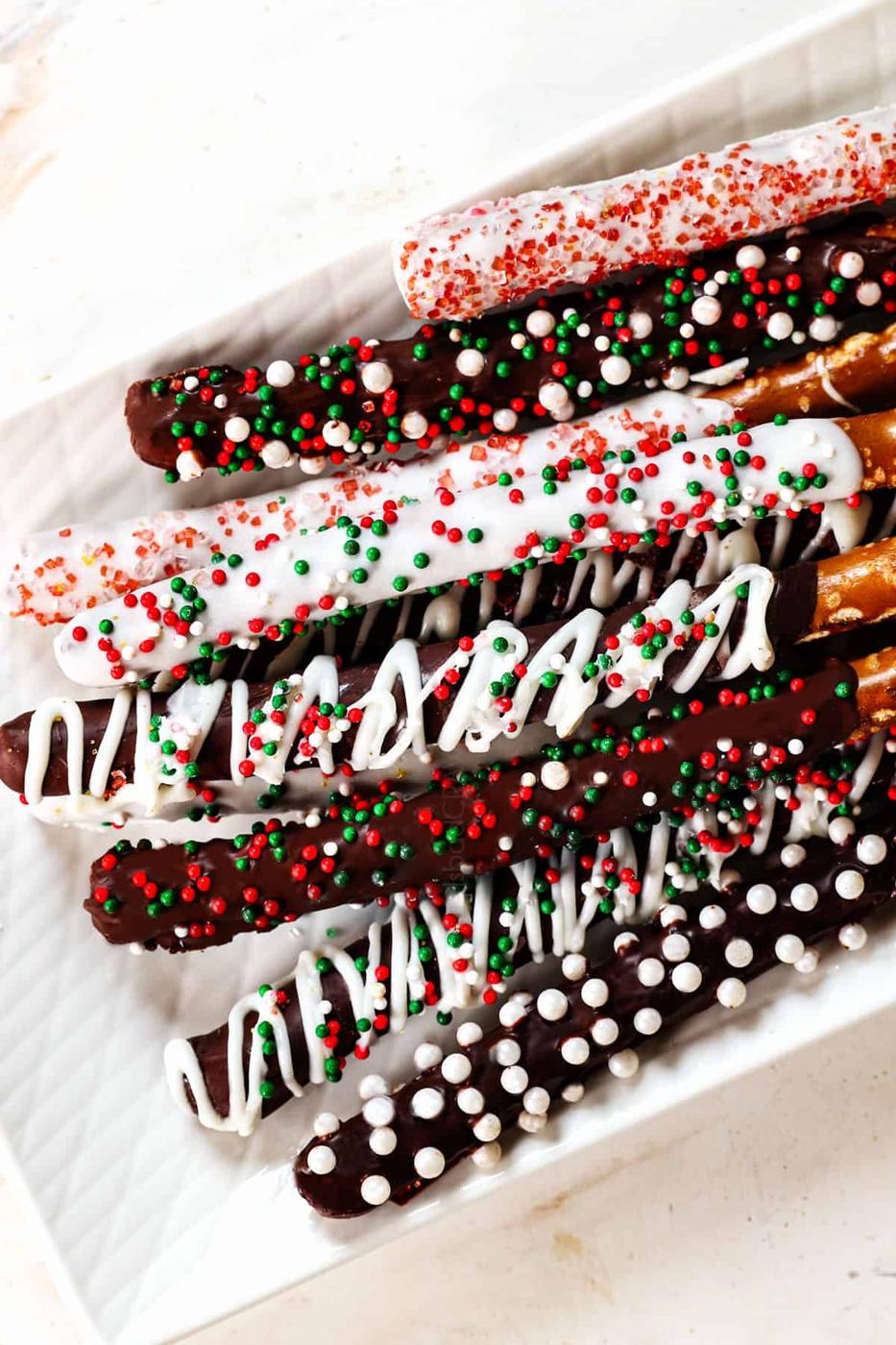Chocolate covered pretzel rods drizzled with white chocolate and topped with crushed candy cane and sprinkles on parchment