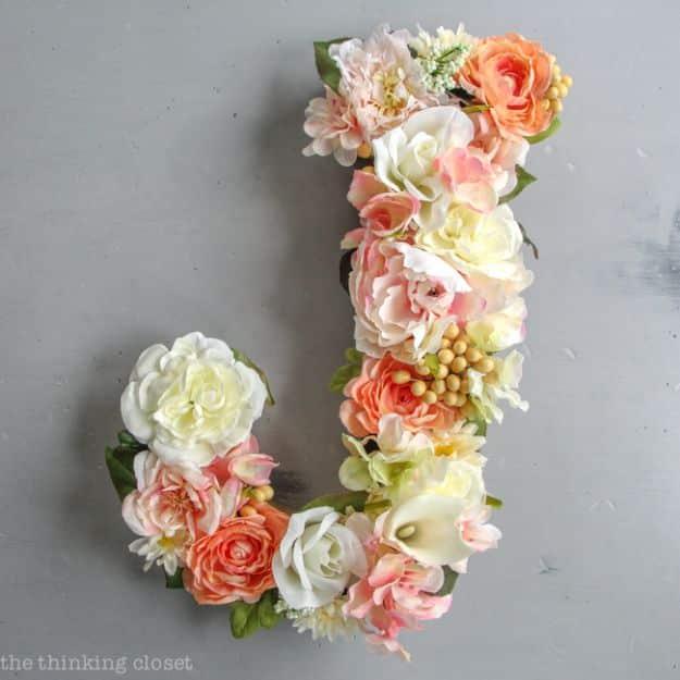 Faux flower monogram letter J in peach, cream and blush blooms mounted on a grey concrete wall as party decor