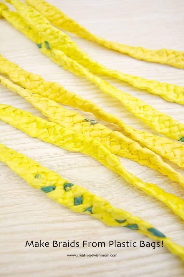 Several lengths of yellow four stranded plastic bag braid laid across a pale wooden table, with green flecks showing