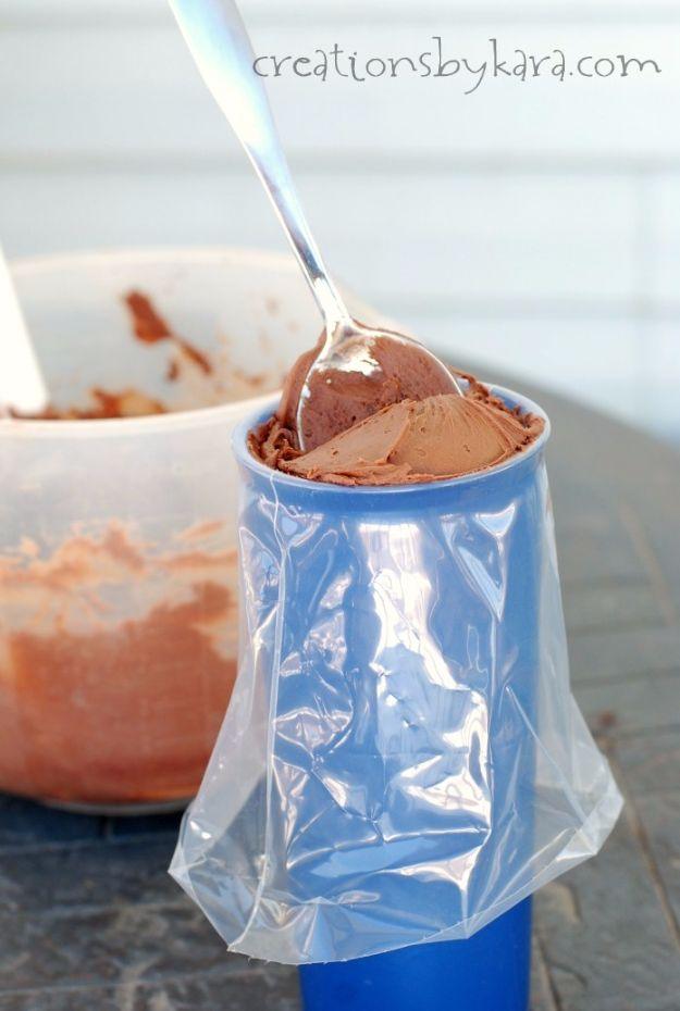 Piping bag folded over the rim of a blue cup being filled with chocolate frosting from a spoon beside a mixing bowl