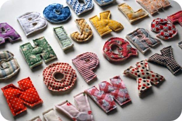 Plush stuffed alphabet letters sewn from fabric scraps in stripes, dots and florals, arranged in rows on grey