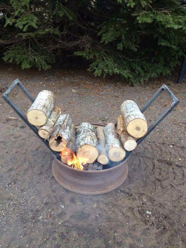 Metal frame holding two angled stacks of split logs leaning over a burning fire pit on gravel in a clearing