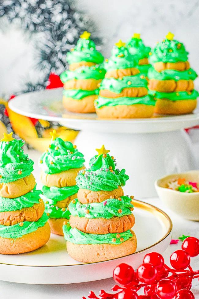 Stacked Christmas tree cookies of three sugar cookies with green buttercream swirls, gold stars and pearls on a cake stand