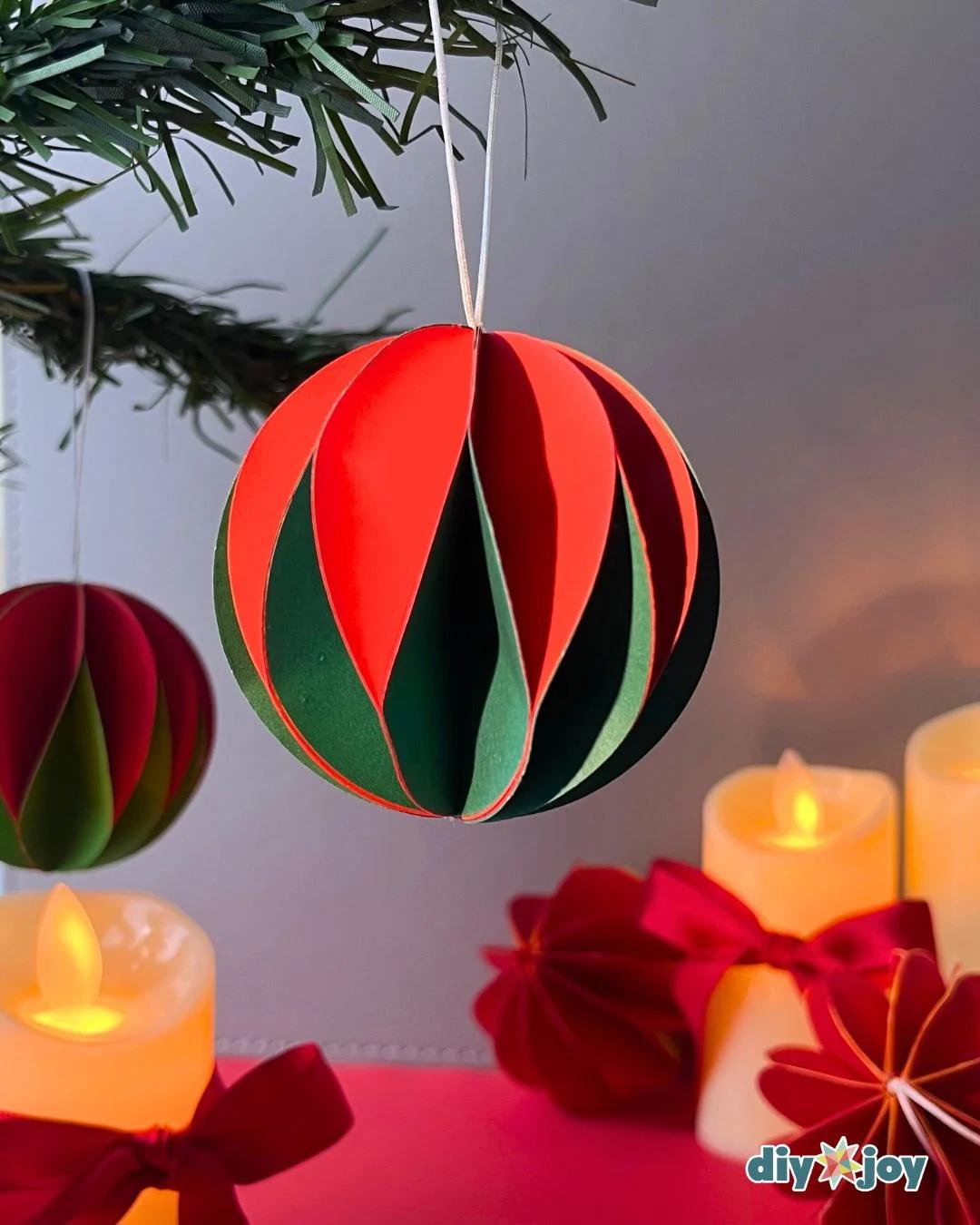 Easy Crafts - a red and dark green striped paper ball ornament hanging from an evergreen branch with lit candles glowing behind it