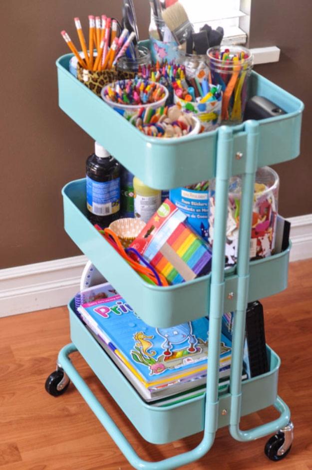 The art cart, a mint three tier rolling cart holding jars of crayons and markers with coloring books on the bottom shelf