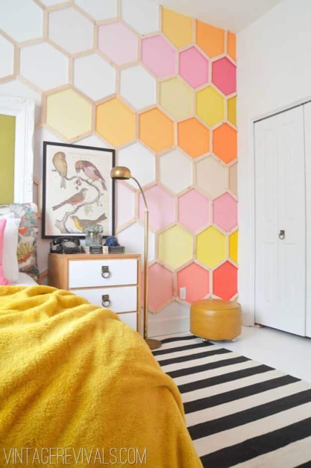Bedroom wall covered in painted hexagons in pink, coral and cream shades beside a bed with a yellow blanket