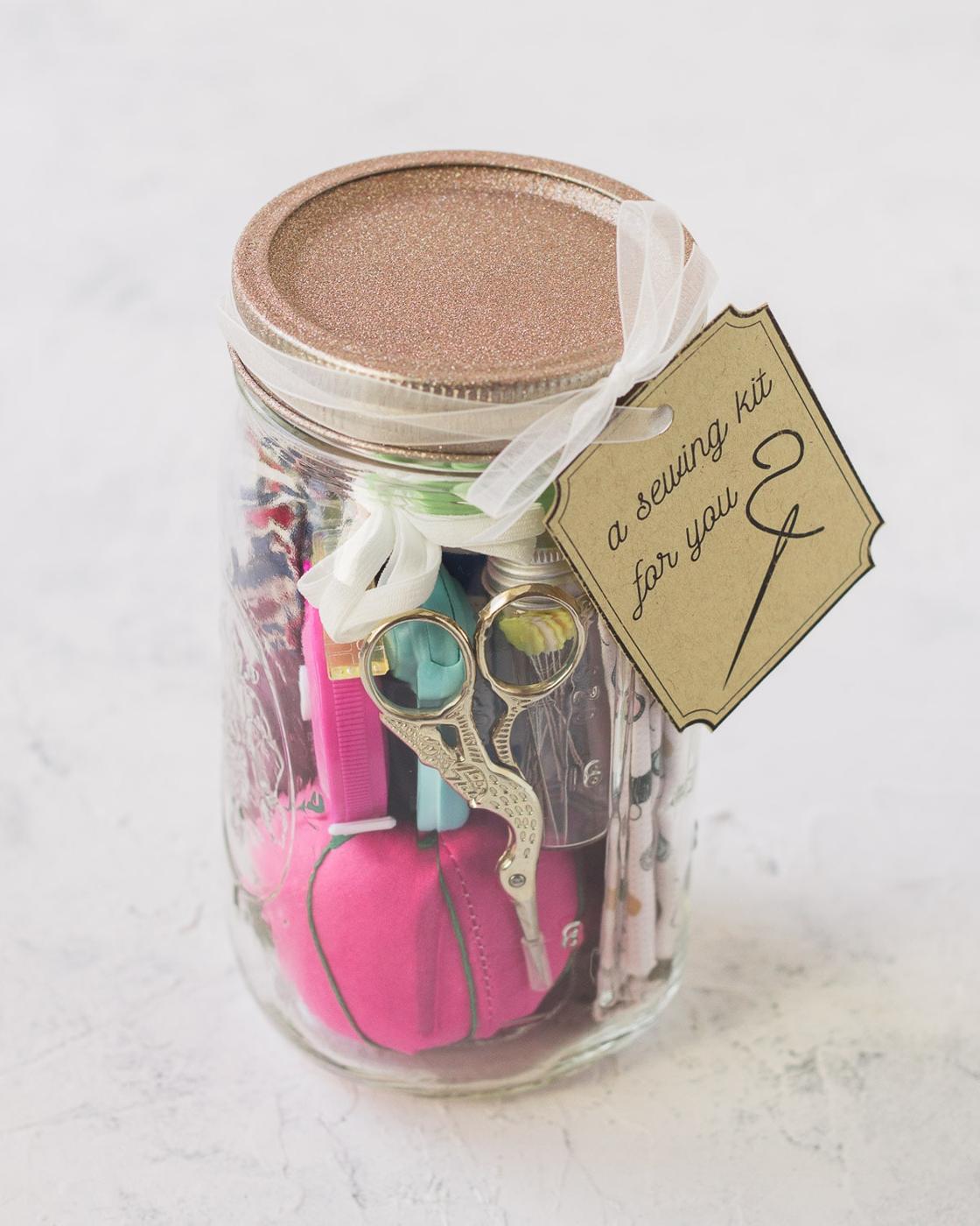Glass mason jar packed with sewing supplies, stork scissors and a pink pincushion, topped with a rose gold lid