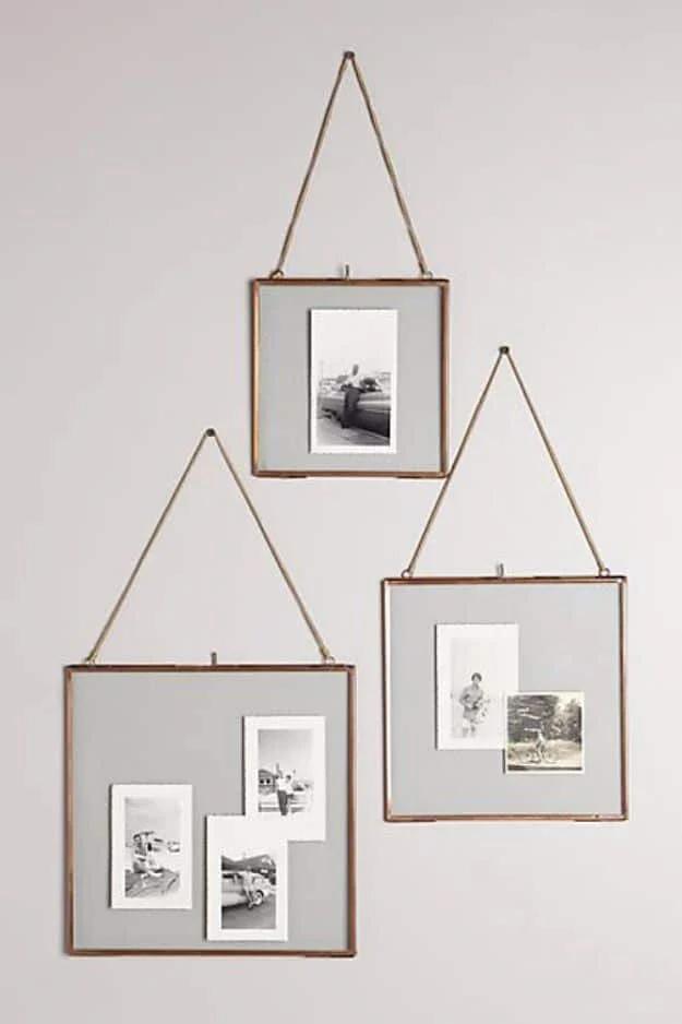 Three brass float frames with glass fronts holding small vintage photos, hanging from thin gold chains against a grey wall