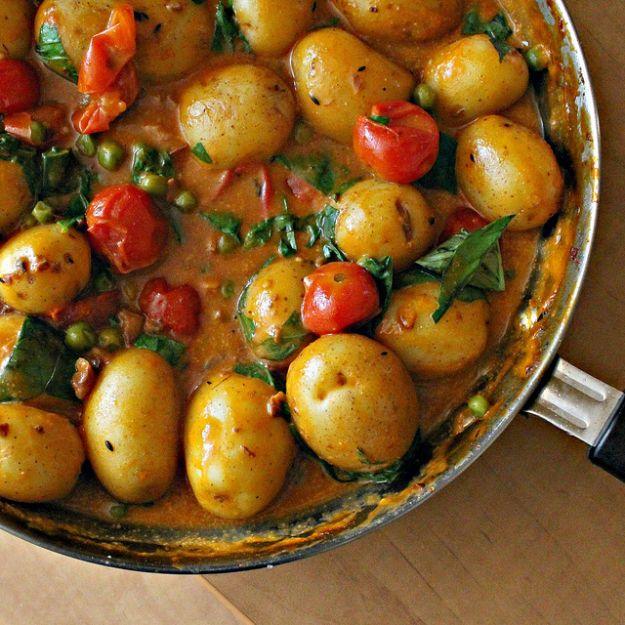 Skillet of coconut potato curry with whole baby potatoes, cherry tomatoes, green peas and fresh basil