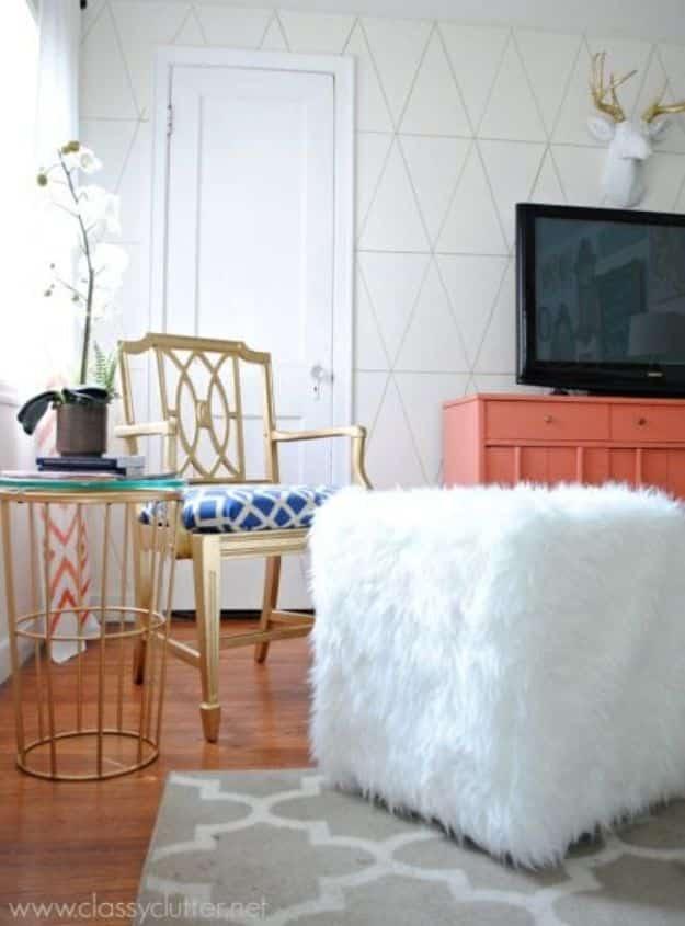 White faux fur cube ottoman on a gray trellis rug beside a gold side table and a gold framed chair, by a coral dresser