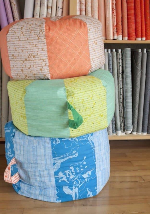Three stacked fabric poufs in coral, mint and blue prints with side handles, sitting in front of a fabric shop shelf