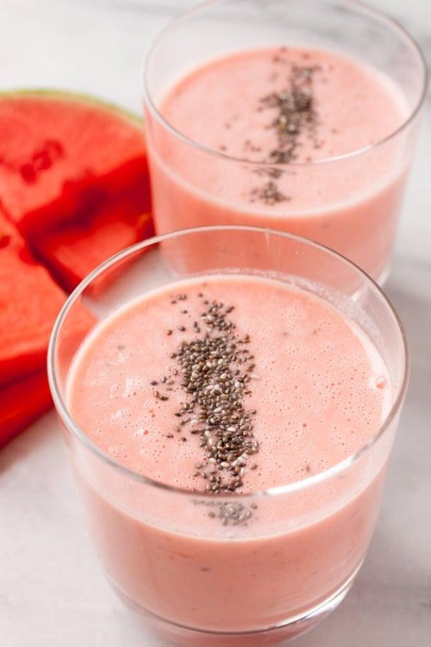Two short glasses of pale pink watermelon smoothie topped with a line of chia seeds beside fresh watermelon slices