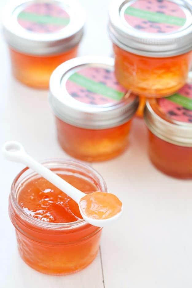 Watermelon jelly in small four ounce canning jars, pale pink and clear, set on a wooden board with melon