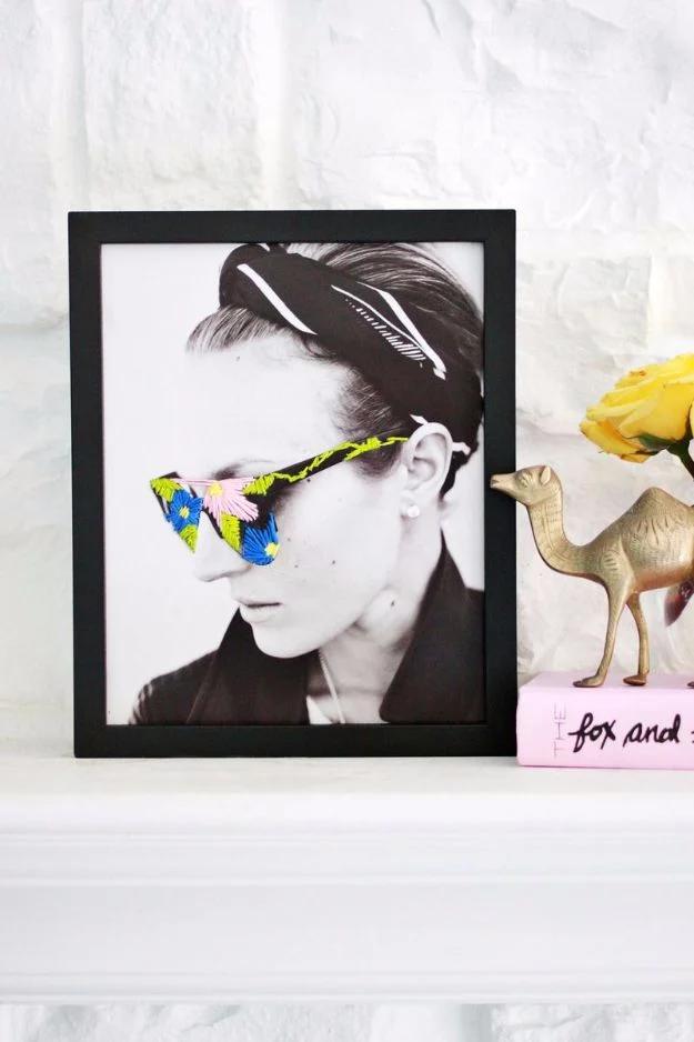 Framed black and white portrait on a mantel with neon pink, blue and yellow flowers embroidered over the sunglasses