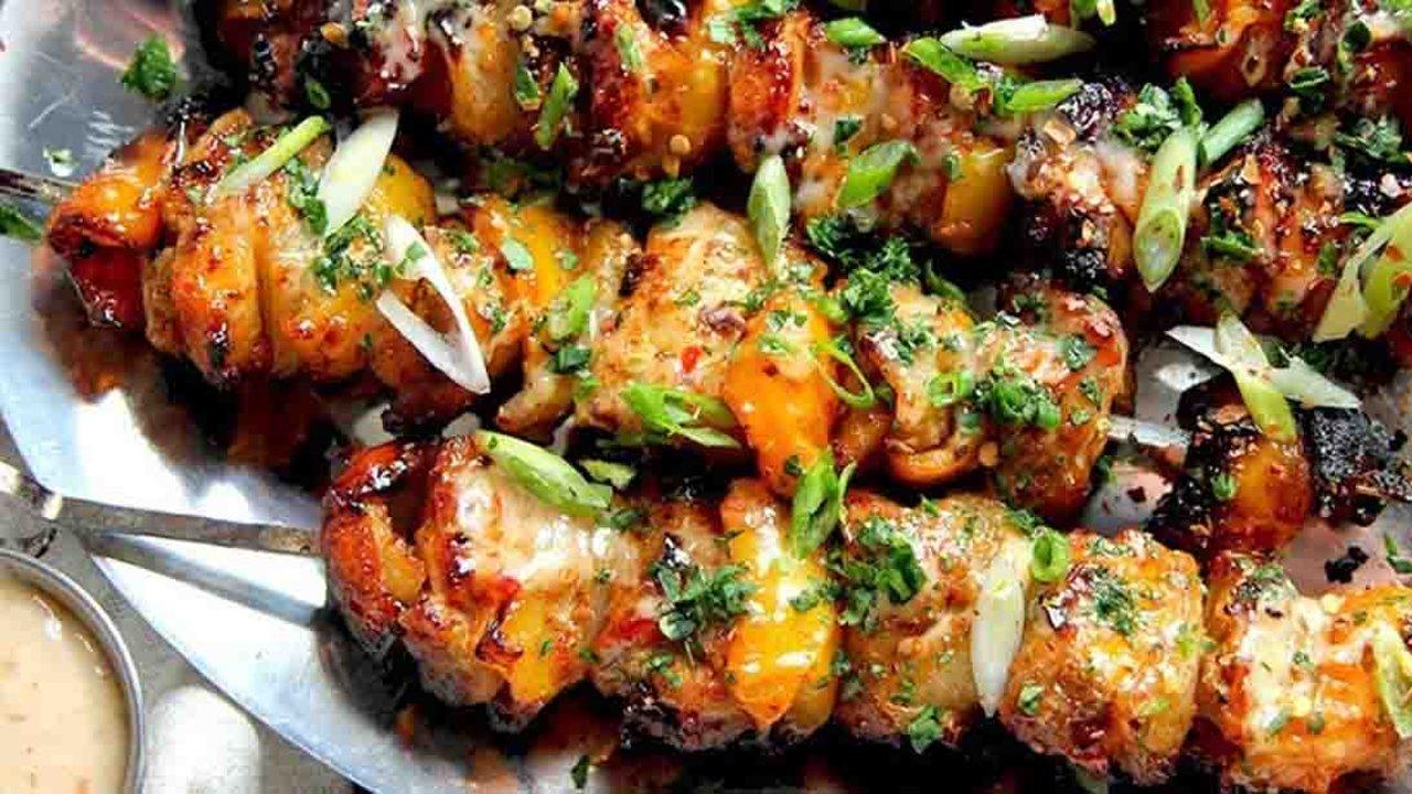 Bang bang chicken skewers with bell pepper and onion chunks drizzled in sweet chili mayo sauce at a backyard cookout