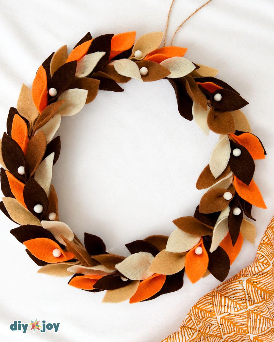 DIY felt fall wreath laid flat, with overlapping brown, cream, and orange leaves and a twine loop for hanging.
