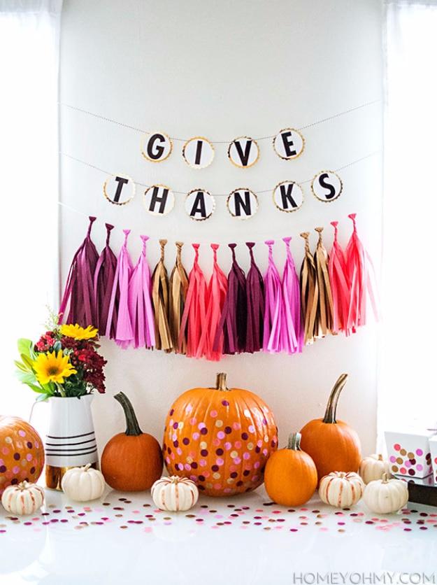 Give thanks banner and tassel garland behind a Friendsgiving buffet table with confetti covered mini pumpkins