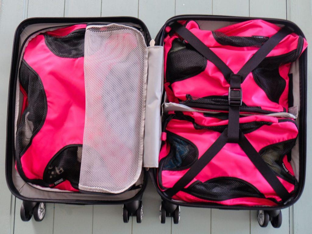 Open black clamshell carry on suitcase with hot pink packing cubes filling both walled halves evenly