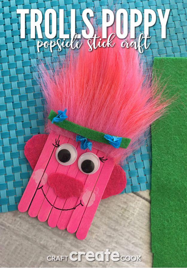 Pink popsicle stick troll face with bright pink faux fur hair, green felt headband, googly eyes and a drawn smile