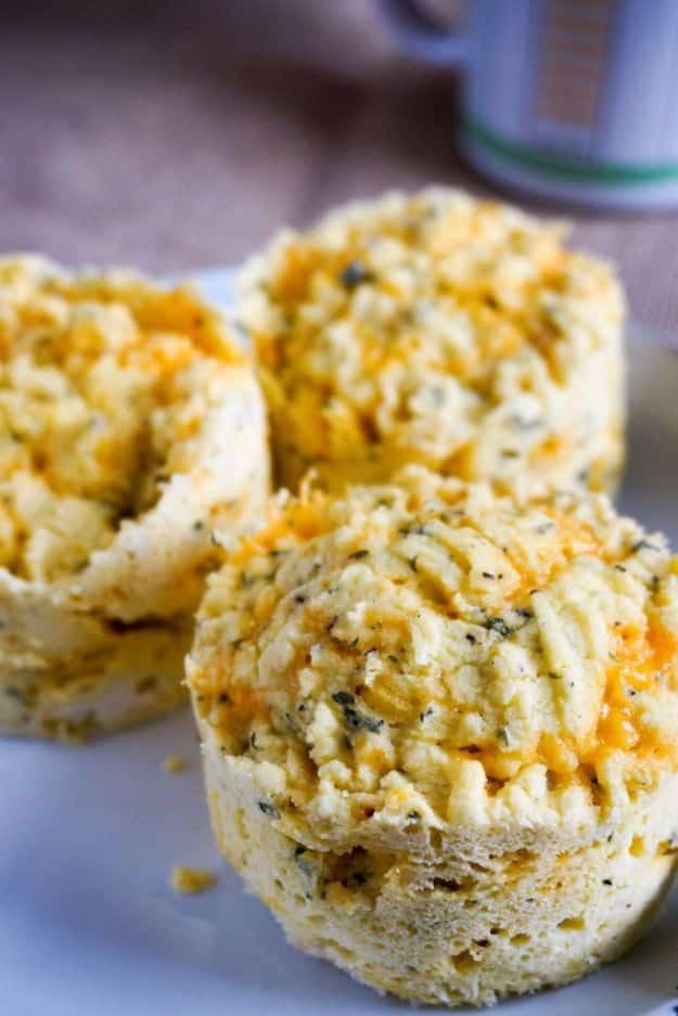 Three round cheesy low carb biscuits flecked with herbs sitting side by side on a pale plate with a blue mug