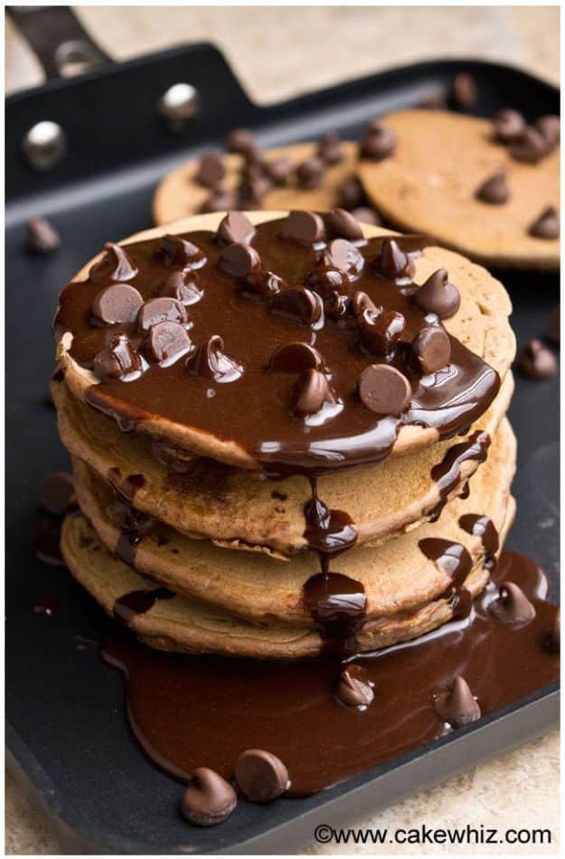 Mocha pancakes stacked on a black griddle with chocolate sauce poured over and chocolate chips on top