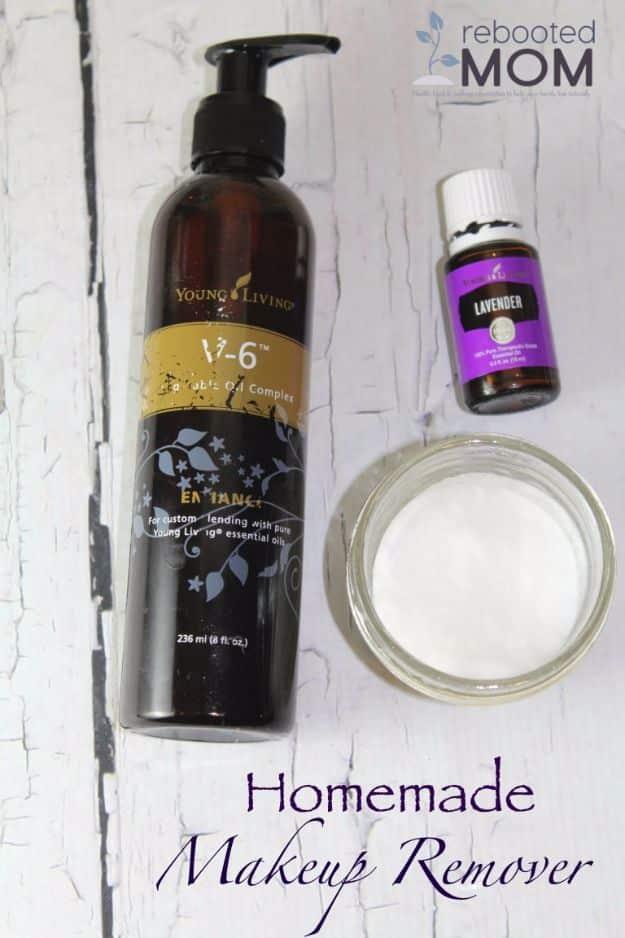 Bottle of carrier oil and lavender essential oil beside a glass jar of cotton rounds on white wood boards