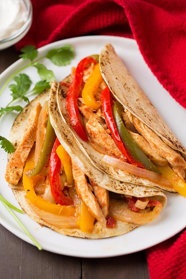 Slow cooker chicken fajitas with red, yellow and green pepper strips in soft tortillas on a white plate