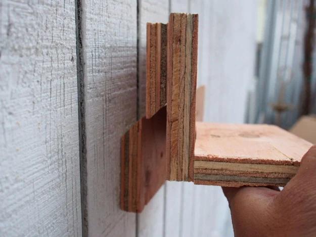 Hands hooking a plywood shelf onto a wall mounted French cleat with matching 45 degree beveled edges
