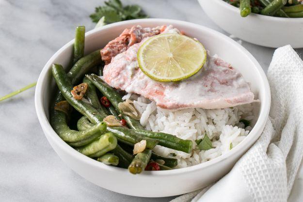 Coconut lime salmon served over white rice and green beans in a shallow white bowl with a lime slice