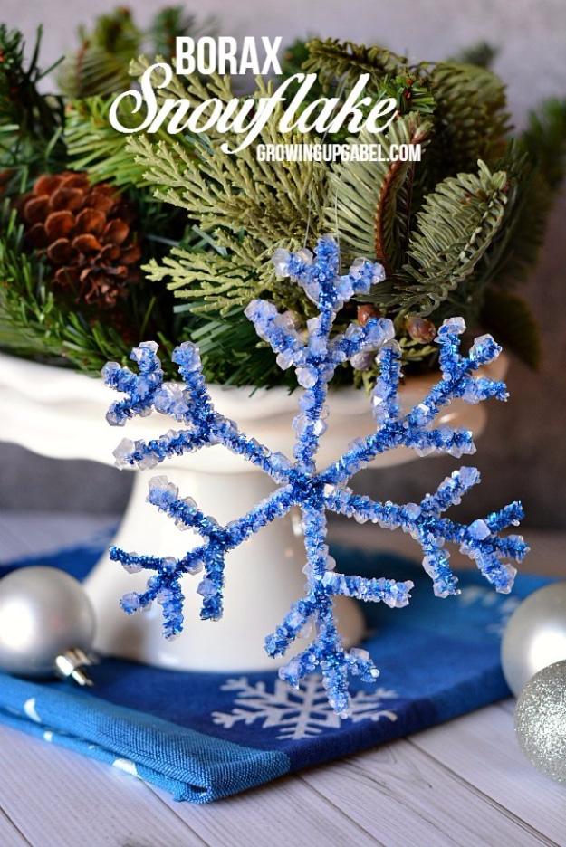Blue borax crystal snowflake resting on a blue napkin in front of evergreen branches and a white pitcher