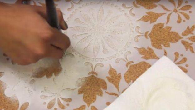 Hand stenciling a gold damask medallion onto a cork board table top with a brush and a large cut stencil