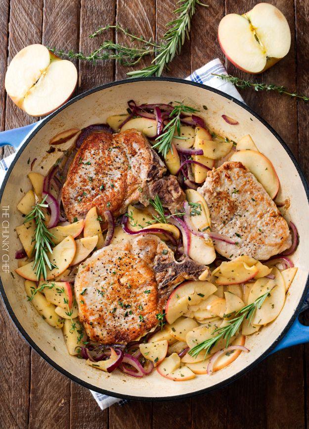 One pan pork chops with sliced apples, red onion and fresh rosemary in a white enamel skillet on wood