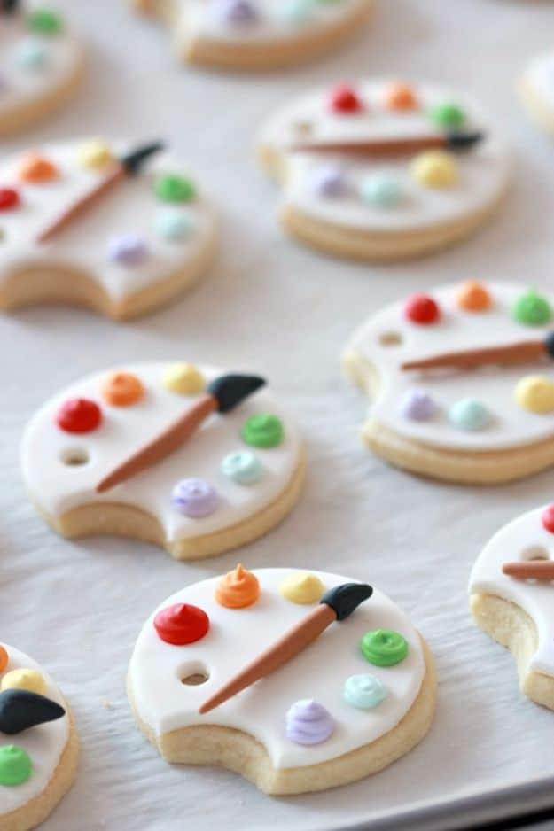 Art palette cookies covered in fondant with colored icing paint blobs and a small fondant paintbrush