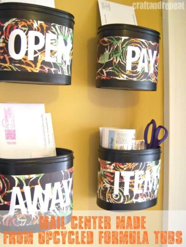Four plastic formula tubs painted black, wrapped in dark patterned paper and labelled in white, hung on a mustard wall