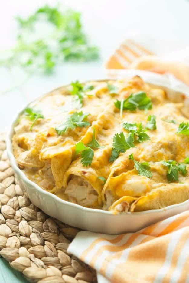 Gluten free chicken enchiladas in a white baking dish under melted cheese with chopped cilantro on top