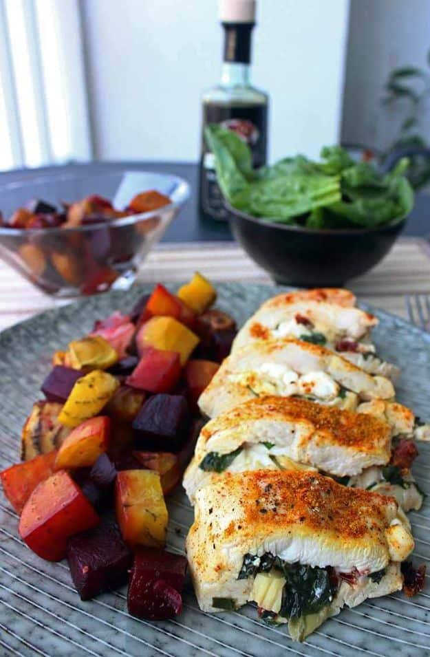 Healthy stuffed chicken breast sliced open showing green filling, served beside roasted beets and root vegetables