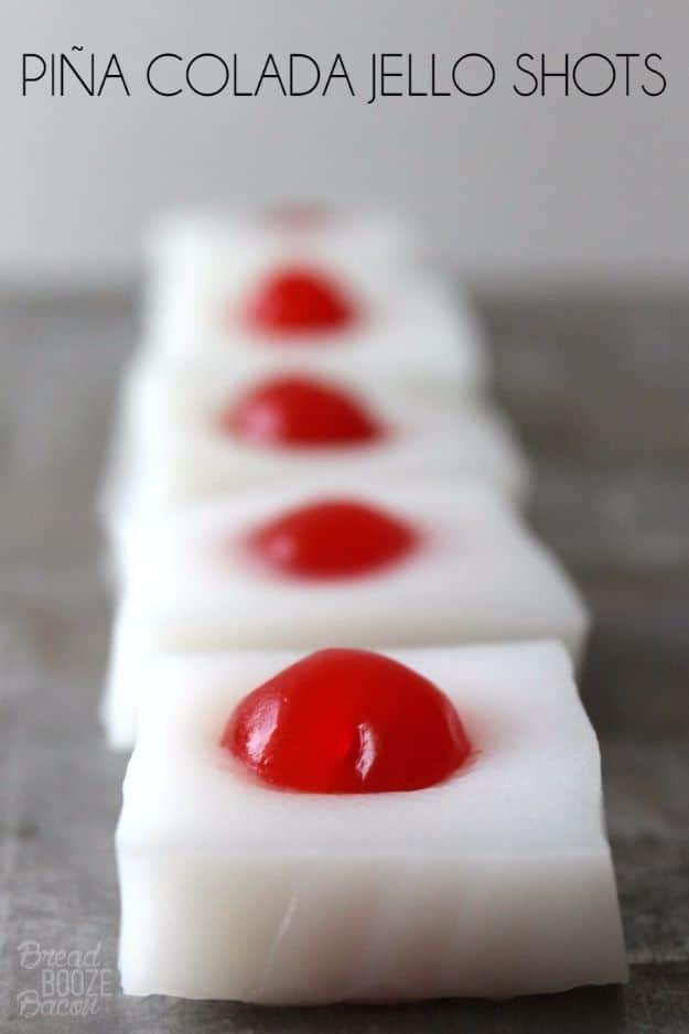 Pina colada jello shots in two ounce cups, each with a maraschino cherry half submerged in the set jello