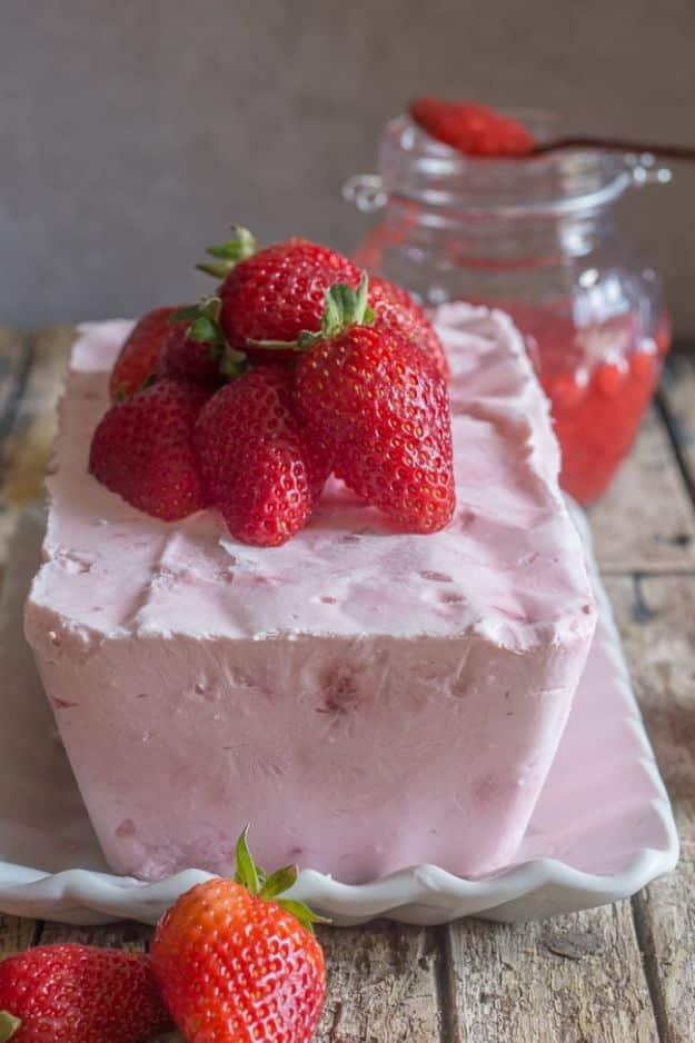 Pink strawberry semifreddo turned out on a white dish, topped with whole strawberries beside a jar of sauce