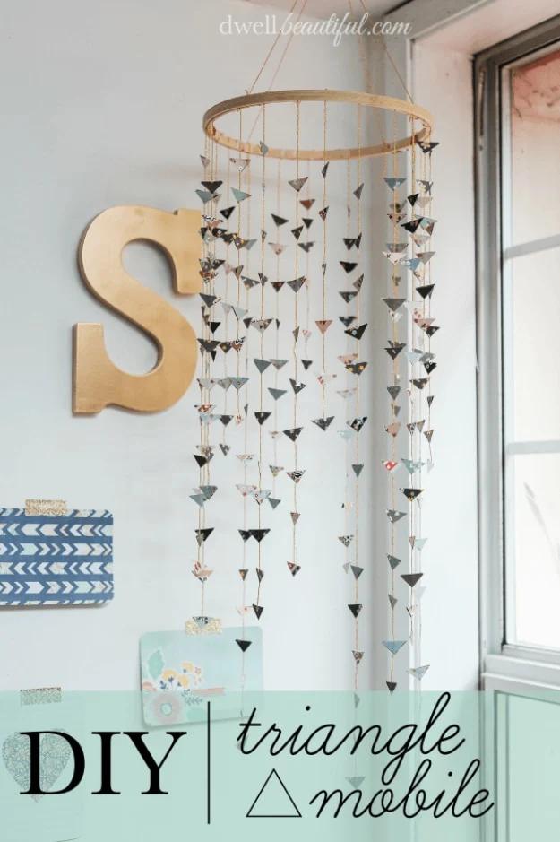 Hanging mobile of small patterned paper triangles on gold string strands from a wooden hoop, beside a gold letter S
