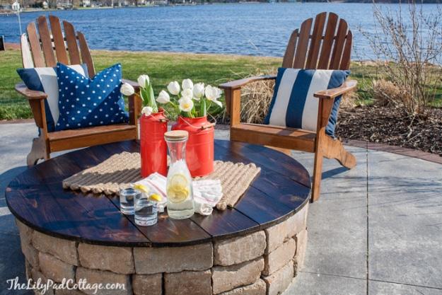 Firepit table top, a round dark stained wooden cover on a stone fire pit set with tulips, candles and glasses