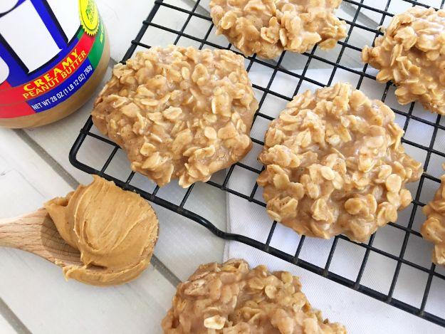 Peanut butter no bake cookies cooling on a black wire rack beside a jar of peanut butter and a spoon