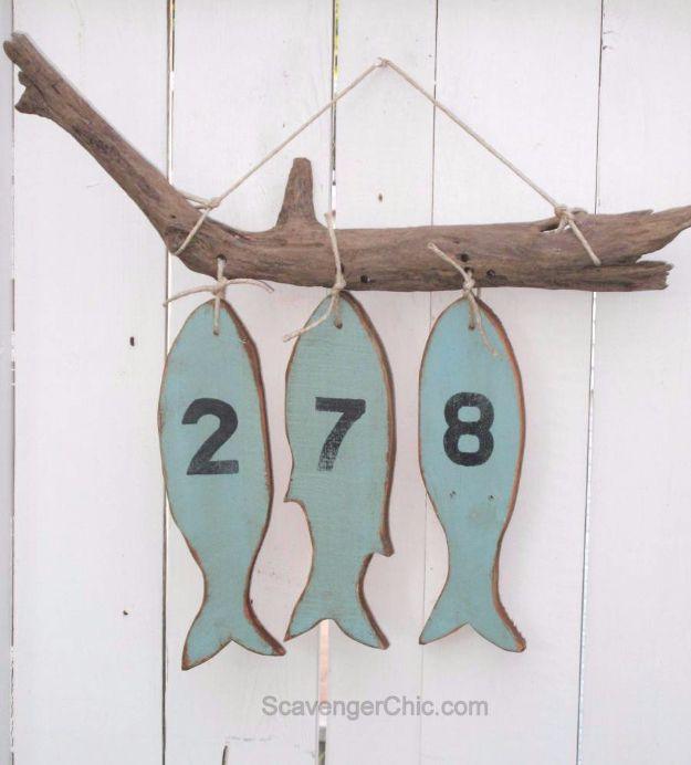 Three wooden fish cut from pallet wood, painted pale blue with numbers, hung from driftwood on jute string