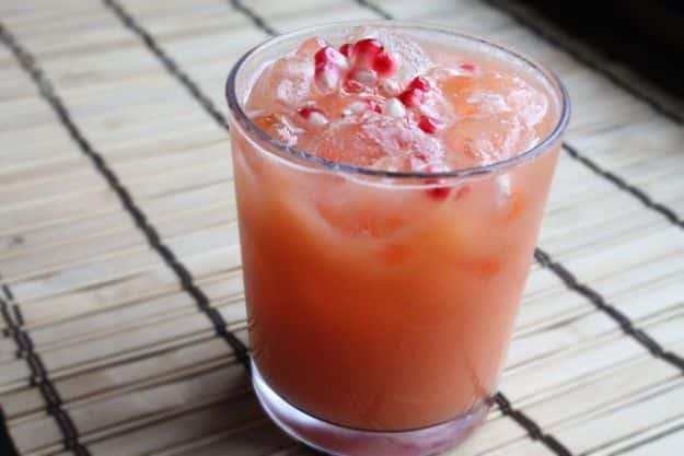 Sweet potato fruit juice poured over ice with pomegranate seeds floating on top, on a rolled bamboo mat