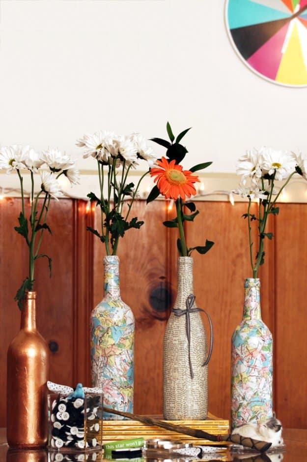 Decoupaged wine bottles, two map collaged bottles beside a copper and a silver one, each holding a single flower