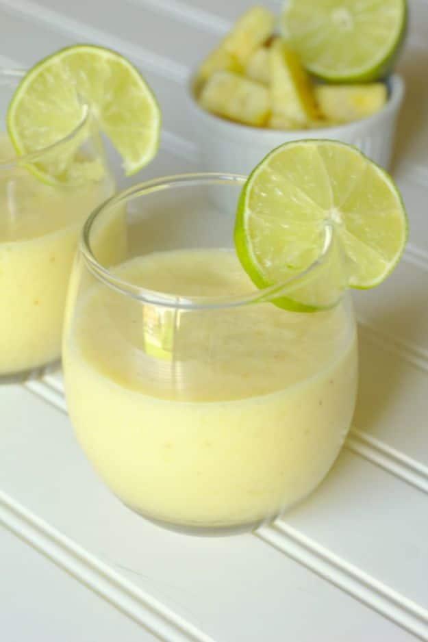 Pina colada lime cooler blended pale and thick with lime wheels on the rims and pineapple chunks behind