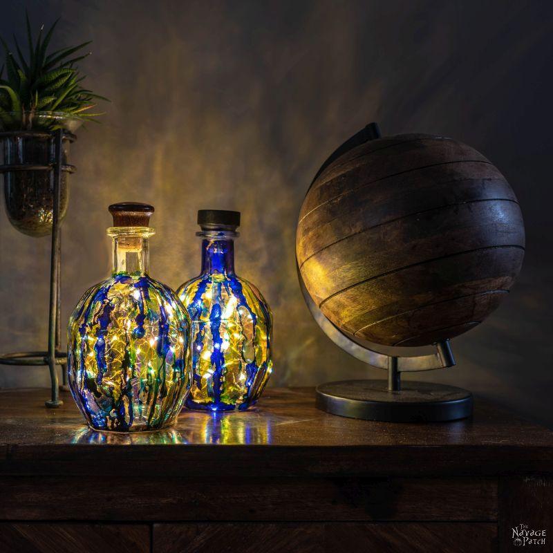 Alcohol ink bottle lights, two squat bottles inked blue and gold glowing on a table beside a large wooden globe